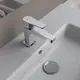 Moderne Waschtischarmatur aus Chrom von Ideal Standard mit einem flachen Hebel und einem runden Abflussstopfen, montiert auf einer weißen Oberfläche.